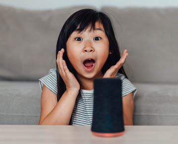 Young Asian girl feeling surprised when talking and listening to smart speaker. Family with smart technology. Smart home can help parents.