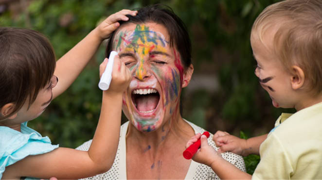 Children painting mother's face with body colours outside - mother seems outrageous