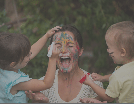 Children painting mother's face with body colours outside - mother seems outrageous
