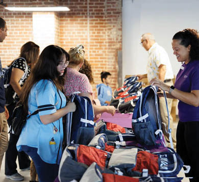 A group of people are gathered around a table with bags on it. A woman is reaching for a bag. There are chairs in the background. AI generated content