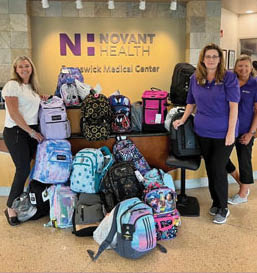 Three women are standing in front of a table full of backpacks. AI generated content